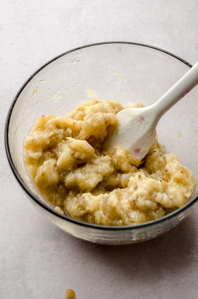A bowl of mashed roasted bananas with a spatula in it.