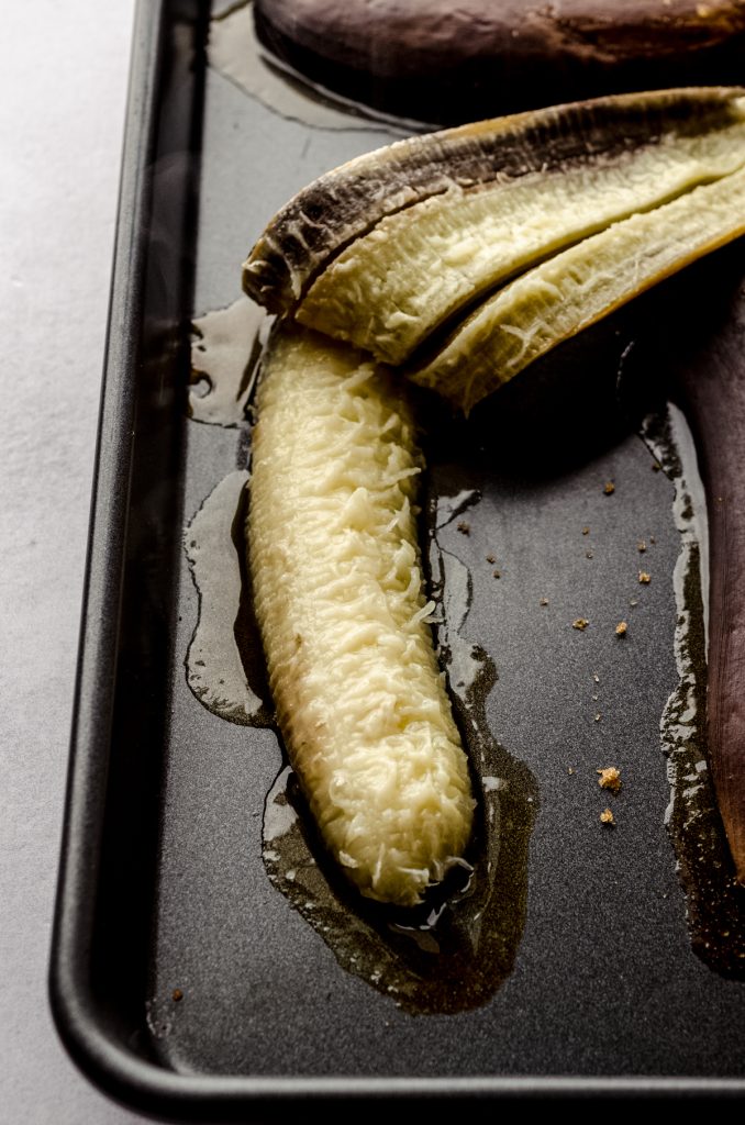 Someone is pulling the black peel off of a baked banana on a baking sheet.