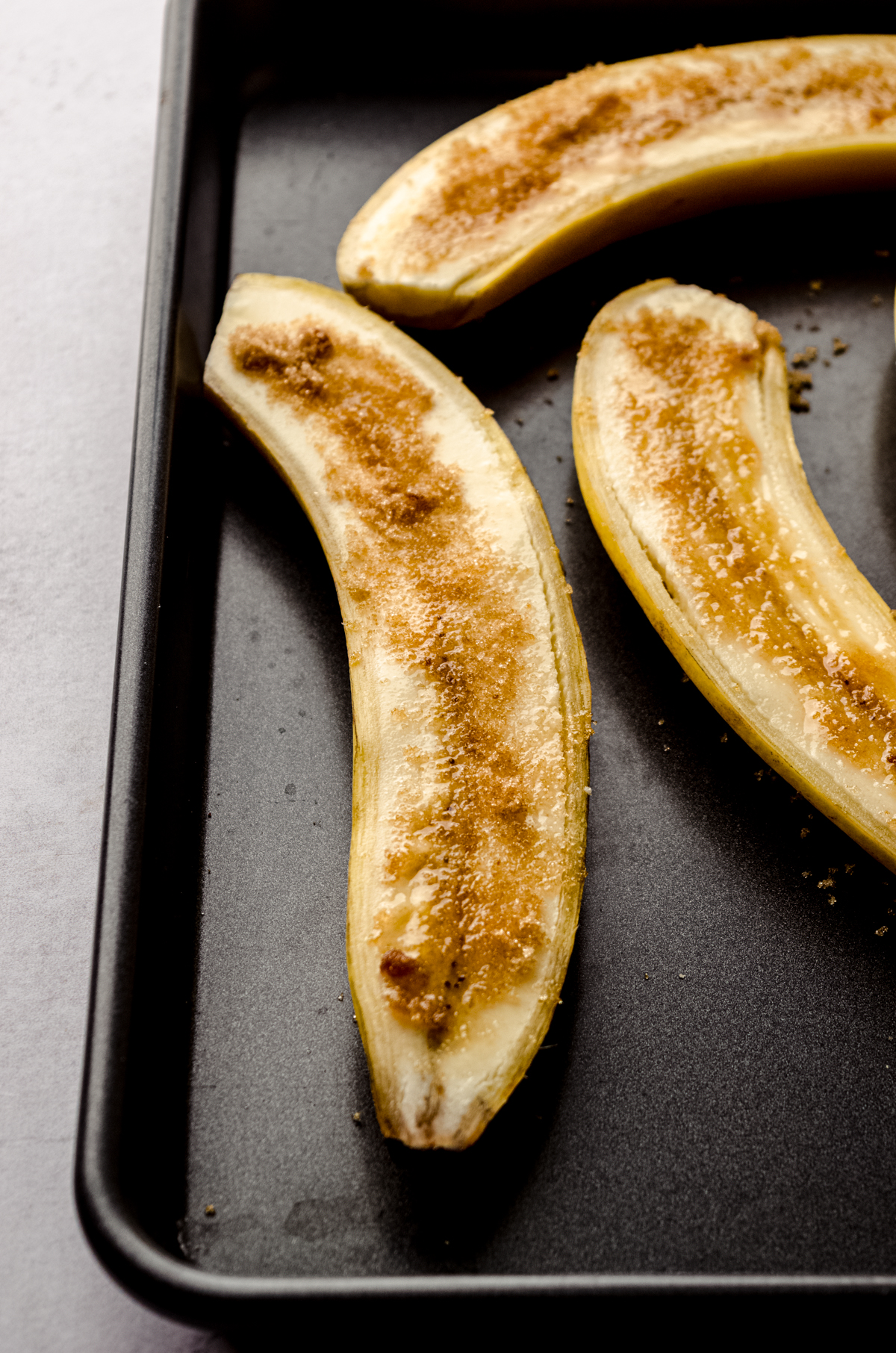 Bananas sliced long ways on a baking sheet sprinkled with brown sugar.