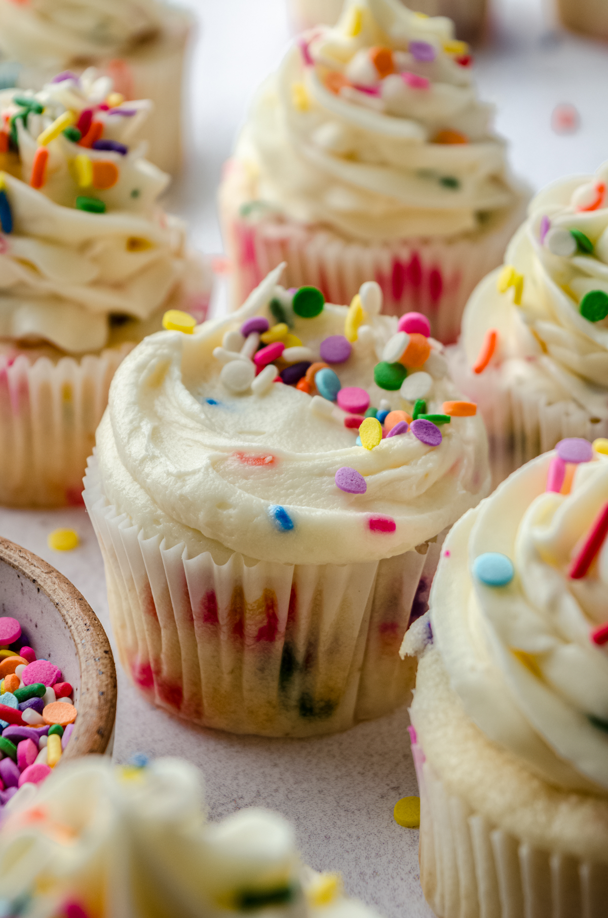 Funfetti cupcakes sitting on a surface with a bowl of sprinkles.