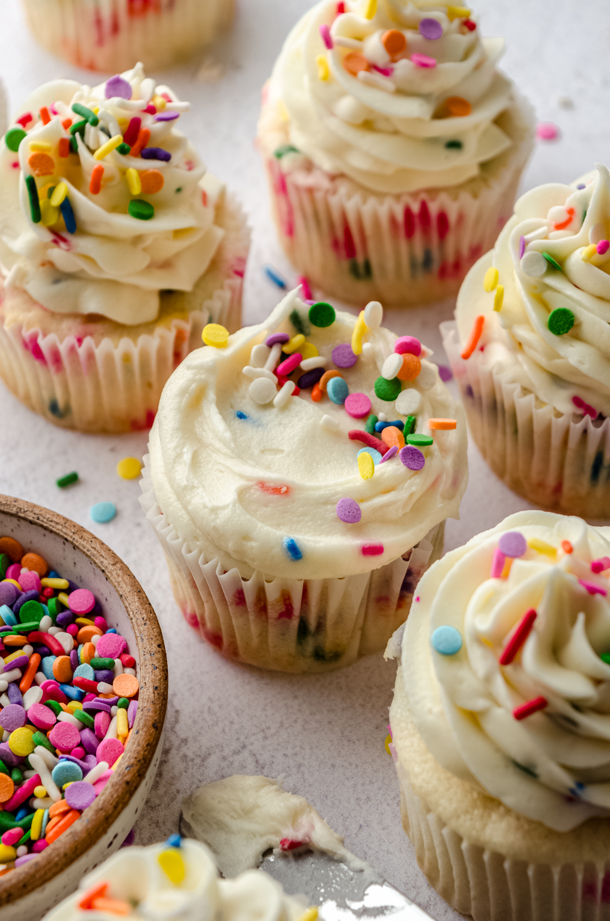 Funfetti cupcakes sitting on a surface with a bowl of sprinkles.