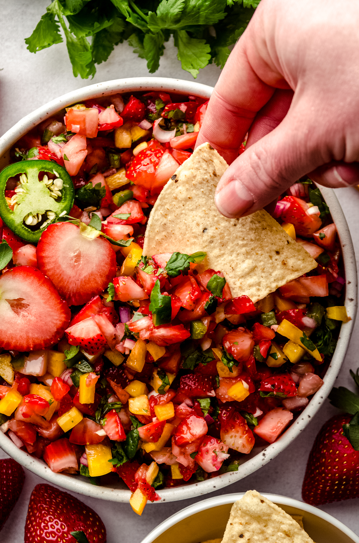 Someone is dipping a tortilla chip into a bowl of fresh strawberry salsa.