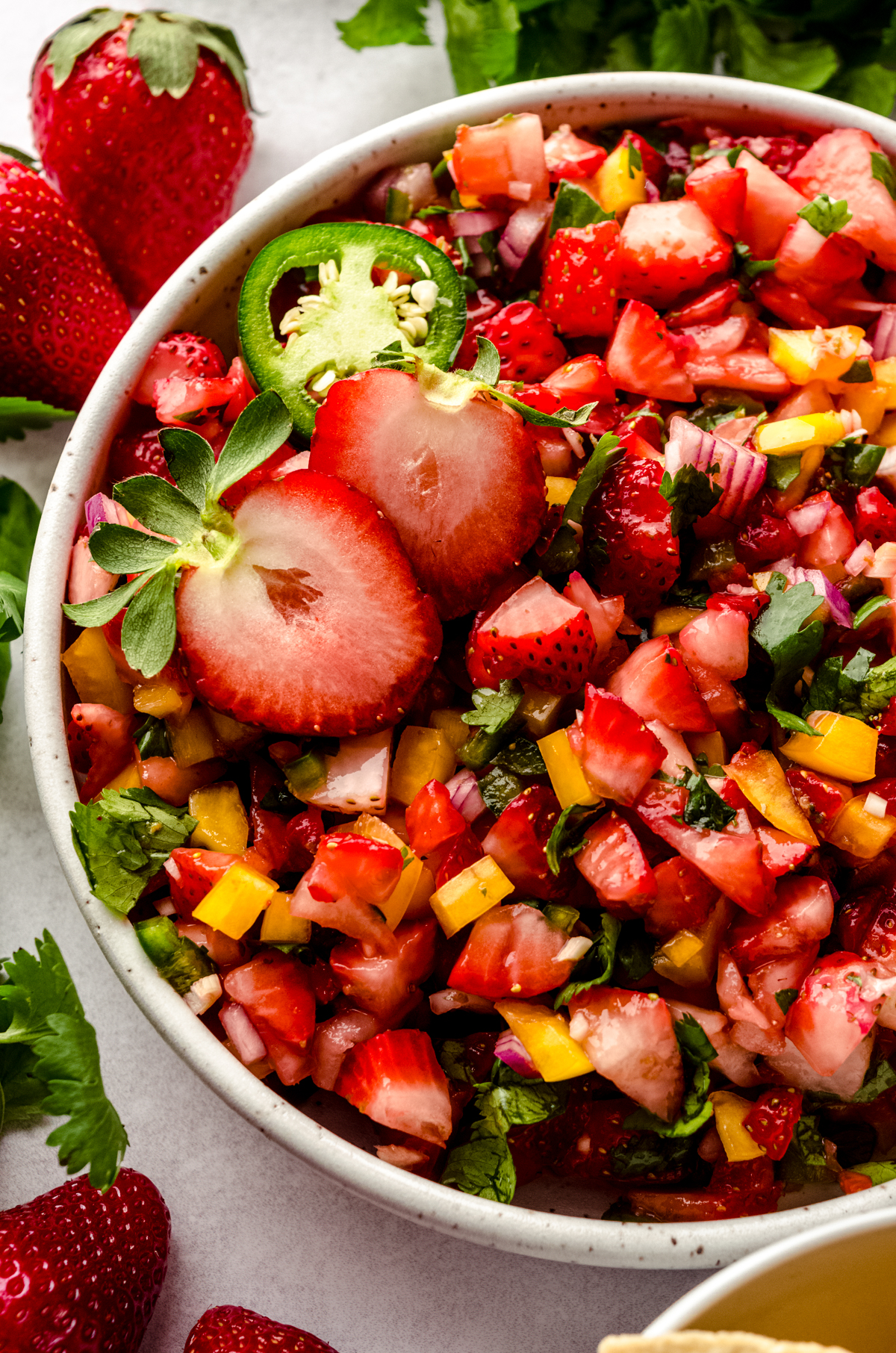 A bowl of fresh strawberry salsa with fresh strawberries and chips around it.