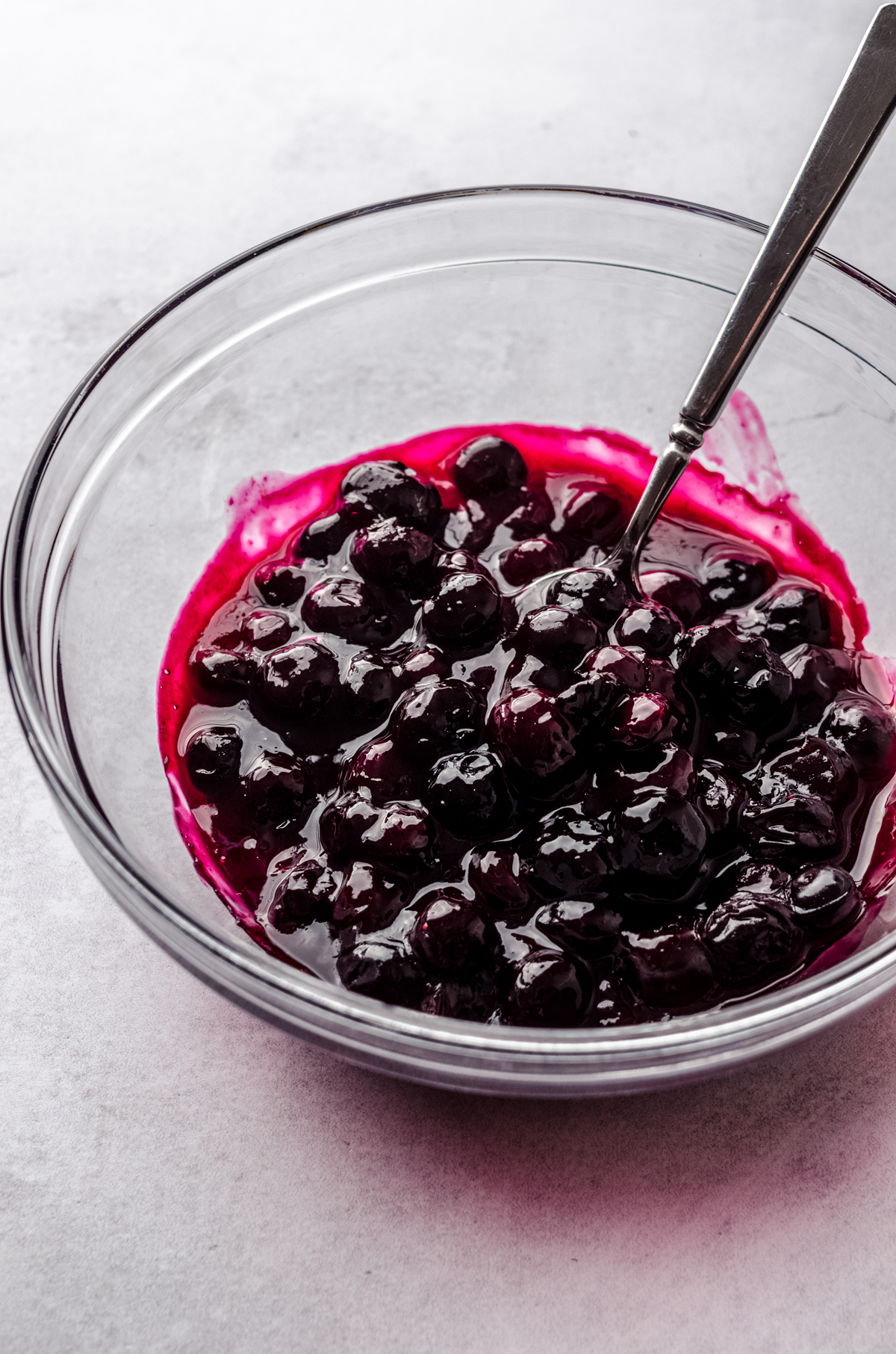 A bowl of blueberry sauce with a spoon for topping lemon blueberry cheesecake.