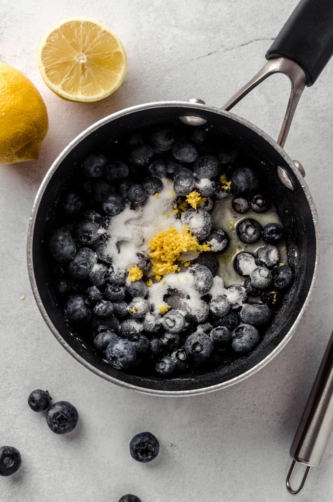 Aerial photo of a saucepan with lemon juice, sugar, lemon zest, and cornstarch in it to start making blueberry sauce for topping lemon blueberry cheesecake.