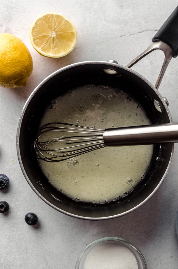 Aerial photo of a saucepan with lemon juice and sugar in it to start making blueberry sauce for topping lemon blueberry cheesecake.