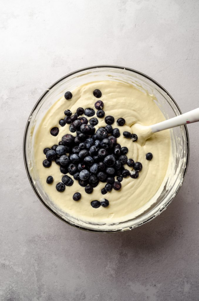 Aerial photo of lemon blueberry cheesecake batter in a large glass bowl with a spatula.