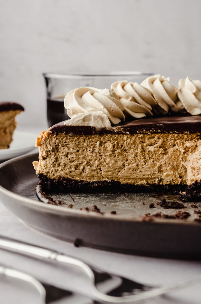 A coffee cheesecake with ganache and coffee whipped cream on top of it sliced so you can see the cross-section of the cheesecake.