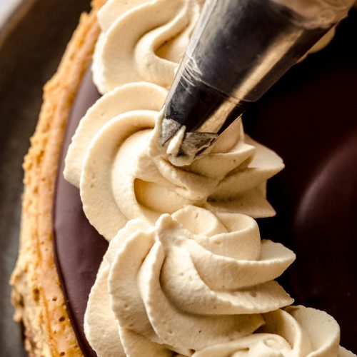 Someone is piping coffee whipped cream onto a coffee cheesecake.