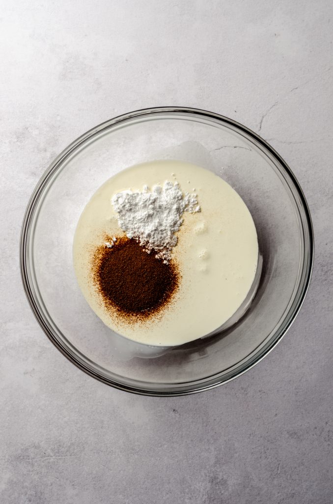 Aerial photo of a bowl of heavy cream with powdered sugar and espresso powder in it to make coffee whipped cream.