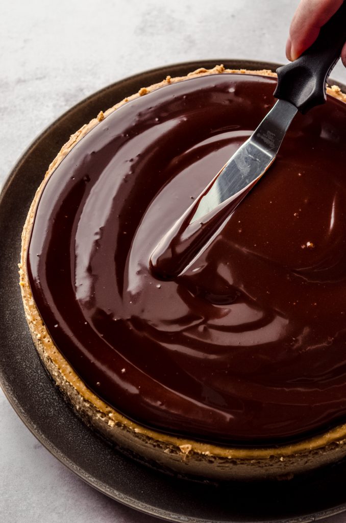 Someone is using a spatula to spread chocolate espresso ganache onto a coffee cheesecake.