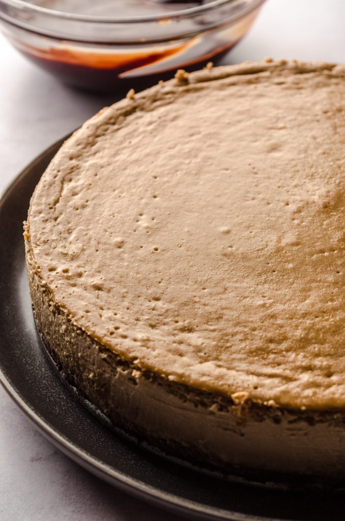 A coffee cheesecake on a plate with a bowl of ganache in the background.