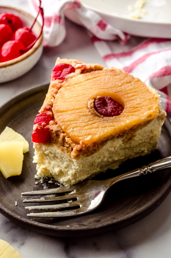 A photo of a slice of pineapple upside down cheesecake on a plate with a fork and a bite taken out of it.