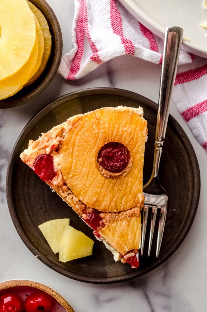 Aerial photo of a slice of pineapple upside down cheesecake sitting on a plate with a fork.