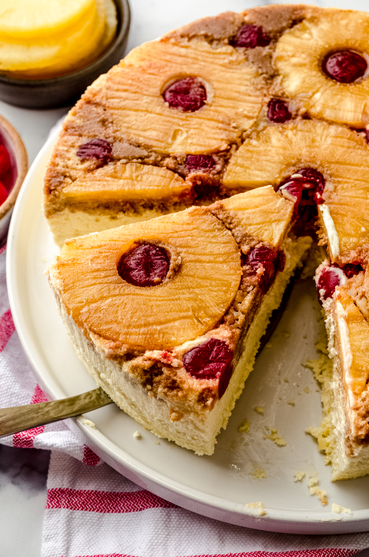 Someone is using a serving utensil to remove a slice of pineapple upside down cheesecake.