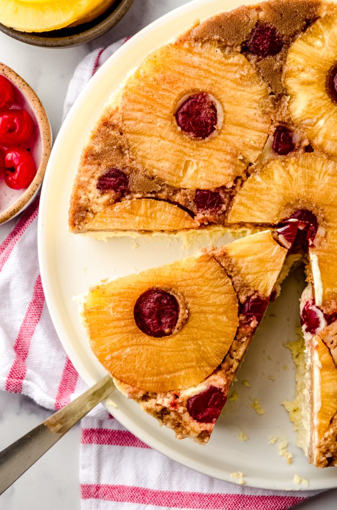 Aerial photo of someone using a serving utensil to remove a slice of pineapple upside down cheesecake.