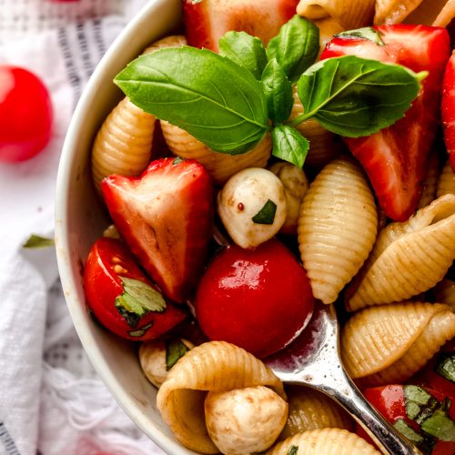 Closeup of a fork in a bowl of strawberry caprese pasta salad in a small white bowl.