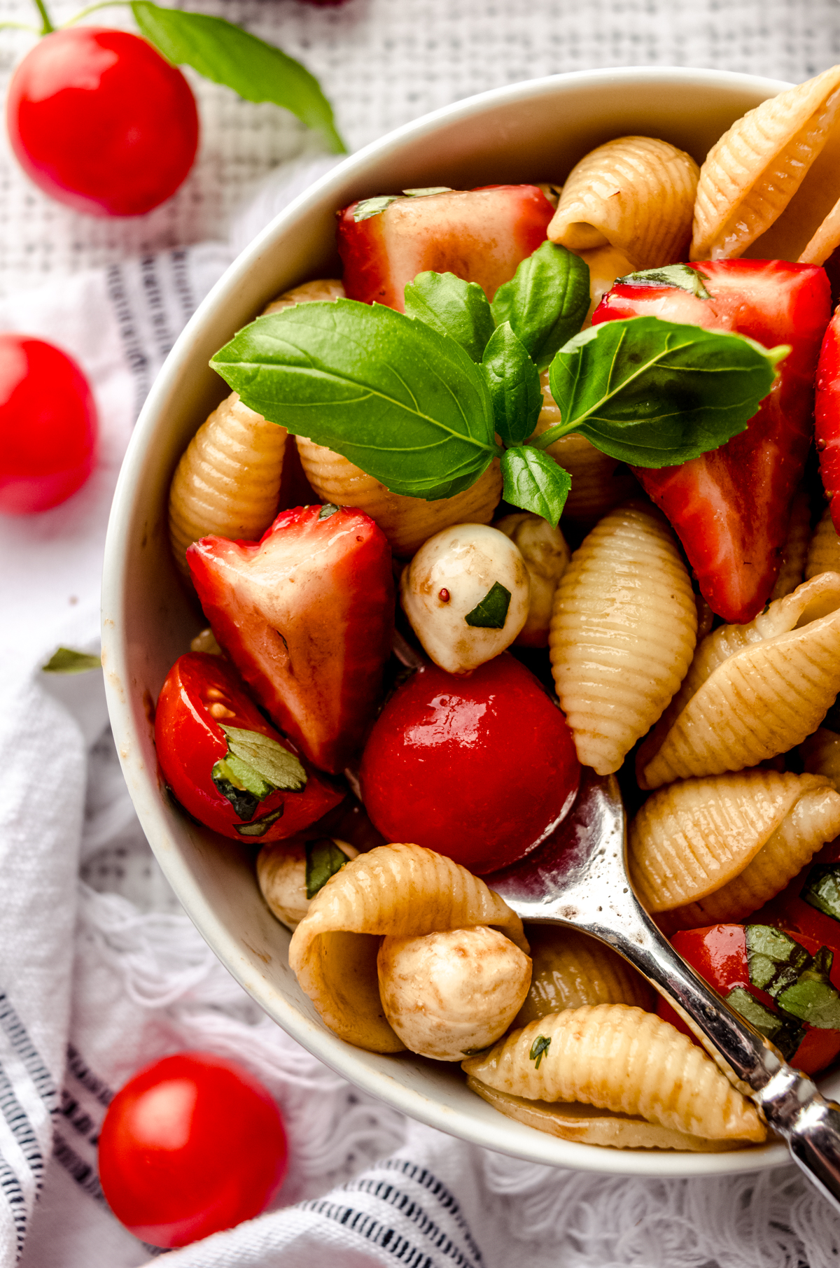 Closeup of a fork in a bowl of strawberry caprese pasta salad in a small white bowl.