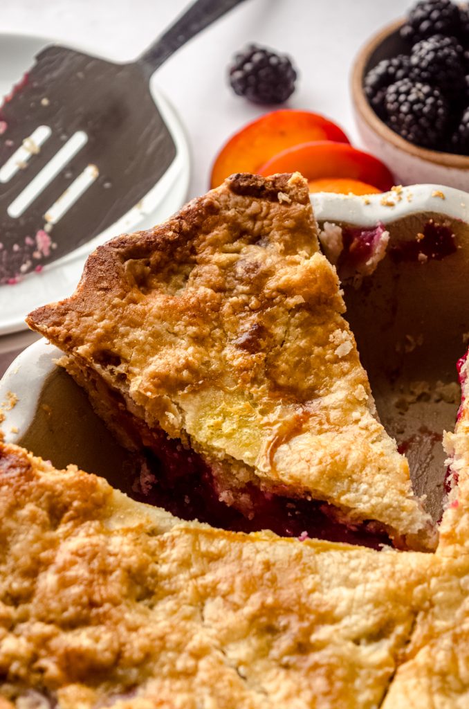 A slice of blackberry peach pie in a pie plate.