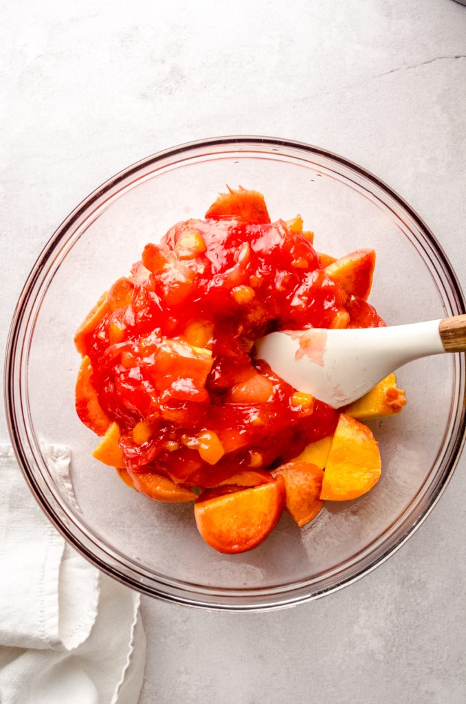 Peaches in a bowl with a spatula ready to make peach blackberry pie.