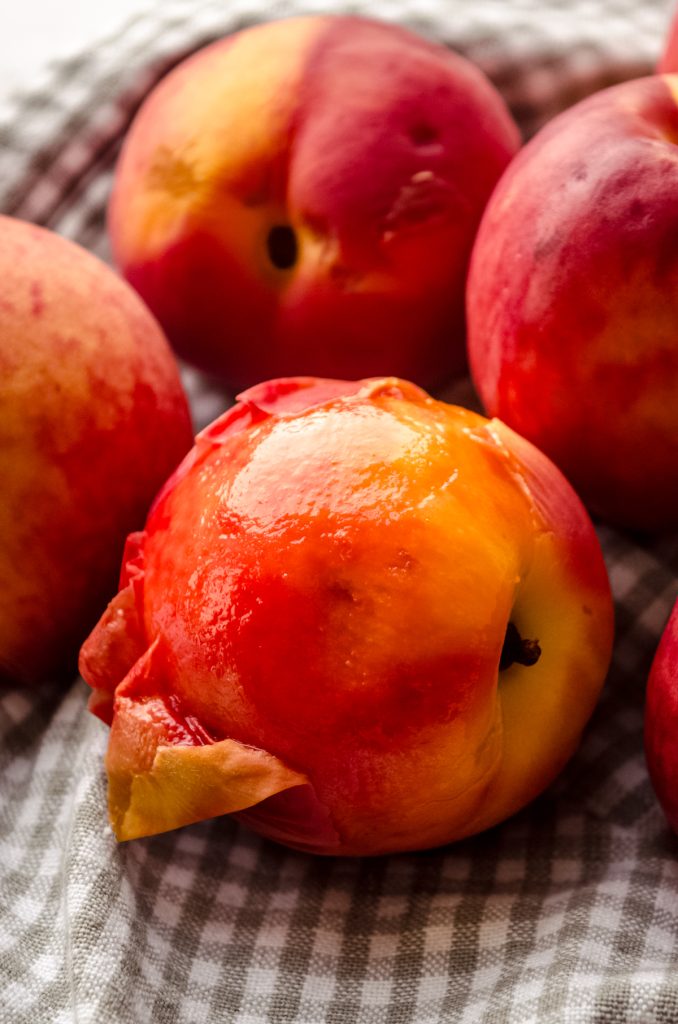 Peaches on a gray and white checkered kitchen towel that have been blanched so they are easy to peel.