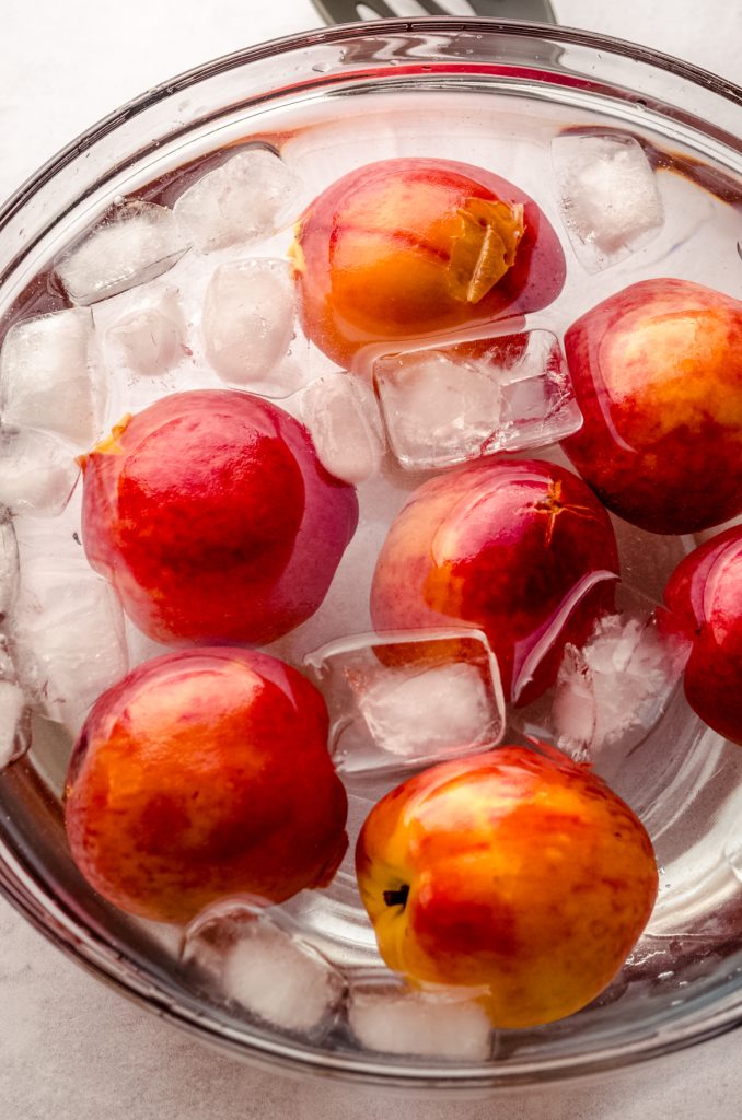 Blanched peaches in a bowl of ice water.