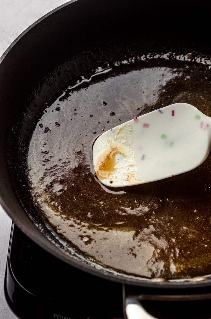 Someone is using a spatula to cook honey and butter to make a honey walnut topping for a goat cheese cheesecake.