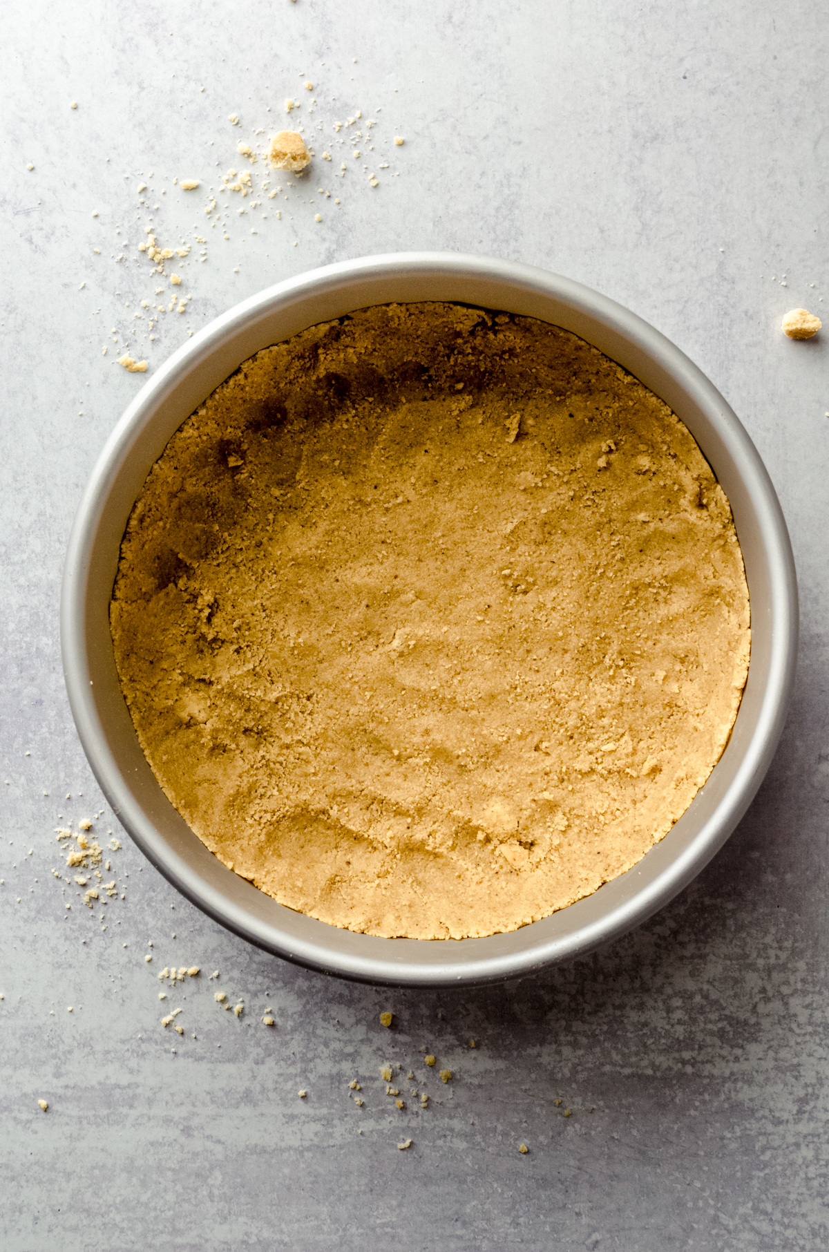 Aerial photo of a shortbread walnut crust in the bottom of a pan to make goat cheese cheesecake.