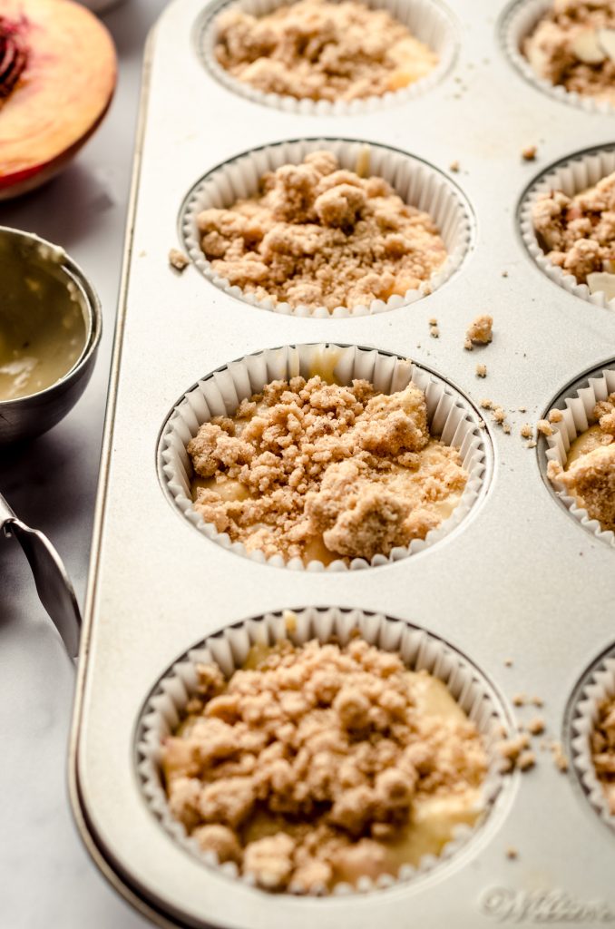 Peach streusel muffins in a muffin pan ready to bake.