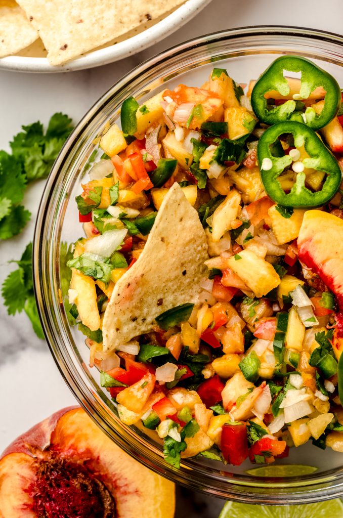 Aerial photo of peach salsa in a large bowl with a chip in it.