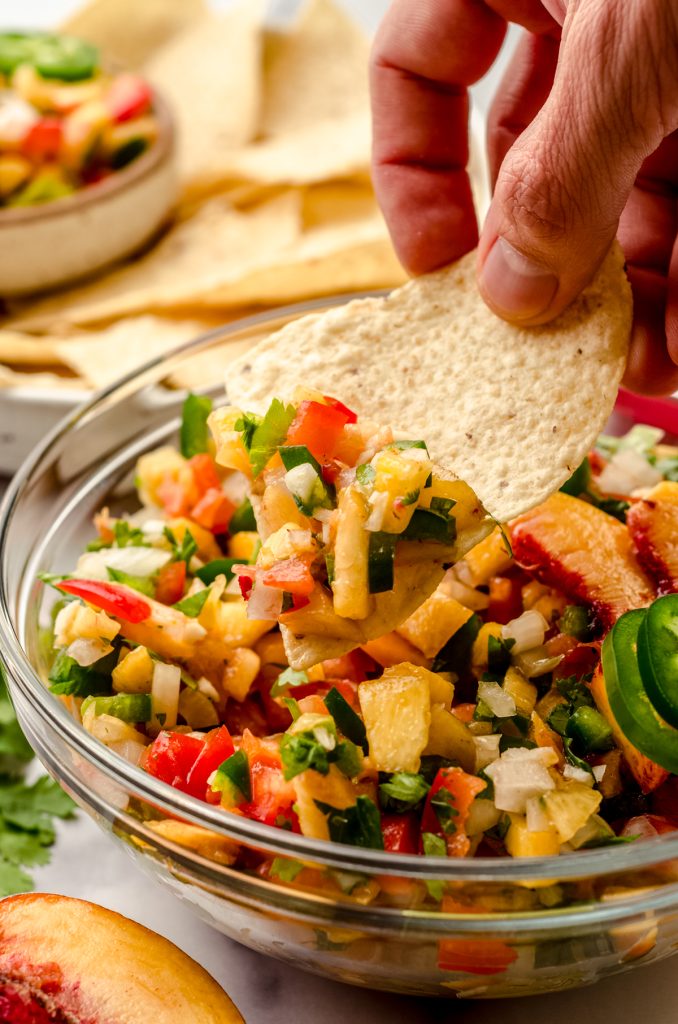 Someone is scooping peach salsa out of a bowl with a tortilla chip.