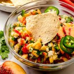 A bowl of peach salsa with a tortilla chip in it.