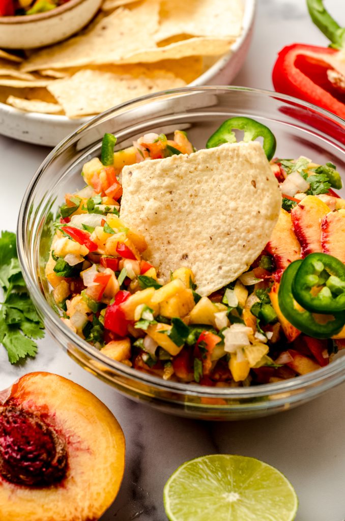 A bowl of peach salsa with a tortilla chip in it.