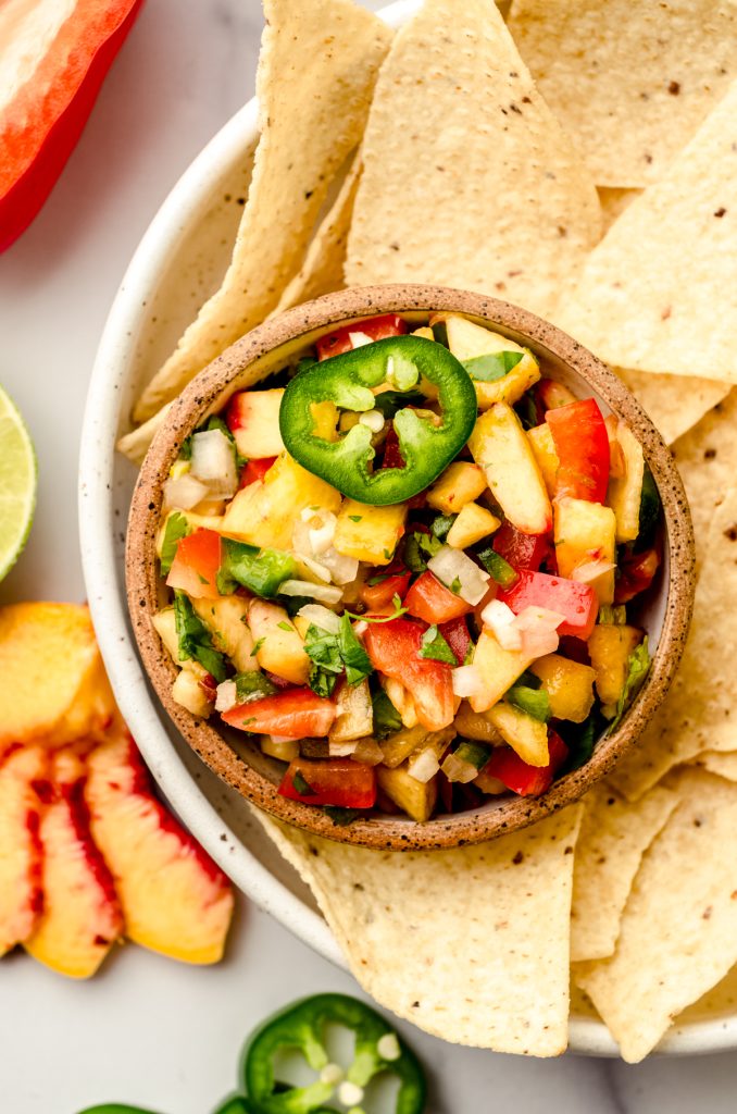 Aerial photo of a small bowl of peach salsa sitting on a plate with tortilla chips.