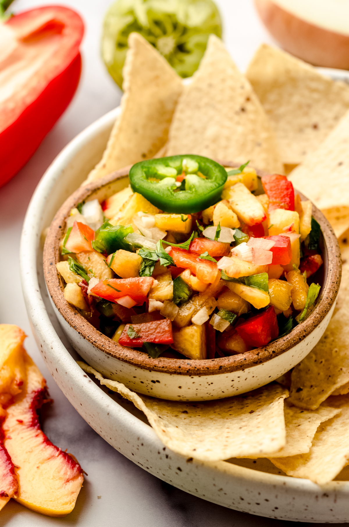 A small bowl of peach salsa sitting on a plate with tortilla chips.