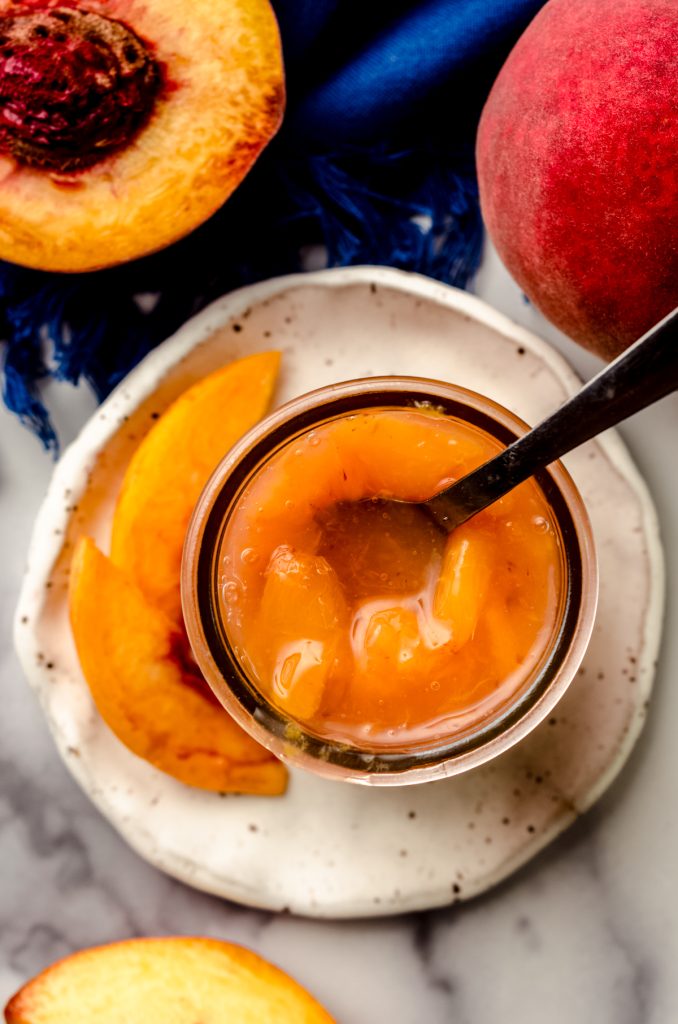 Aerial photo of a jar of peach compote on a plate with a small spoon in it.