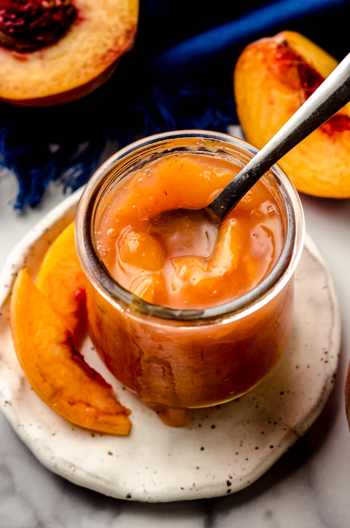 A jar of peach compote on a plate with a small spoon in it.