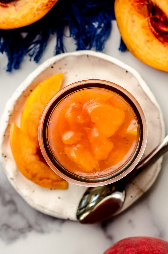 Aerial photo of a jar of peach compote on a plate with a small spoon.