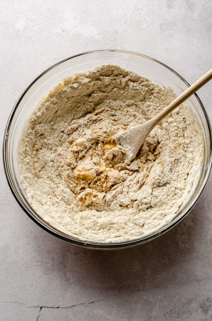 A progress photo of the ingredients make pumpkin cinnamon rolls being mixed in a large bowl with a wooden spoon.