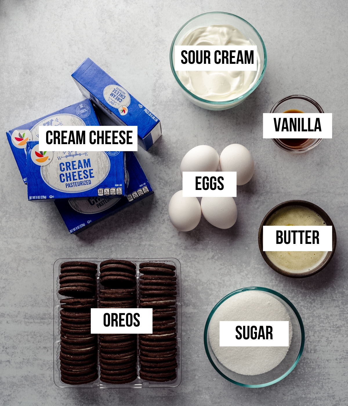 Aerial photo of ingredients to make cookies and cream cheesecake with text overlay labeling each ingredient.