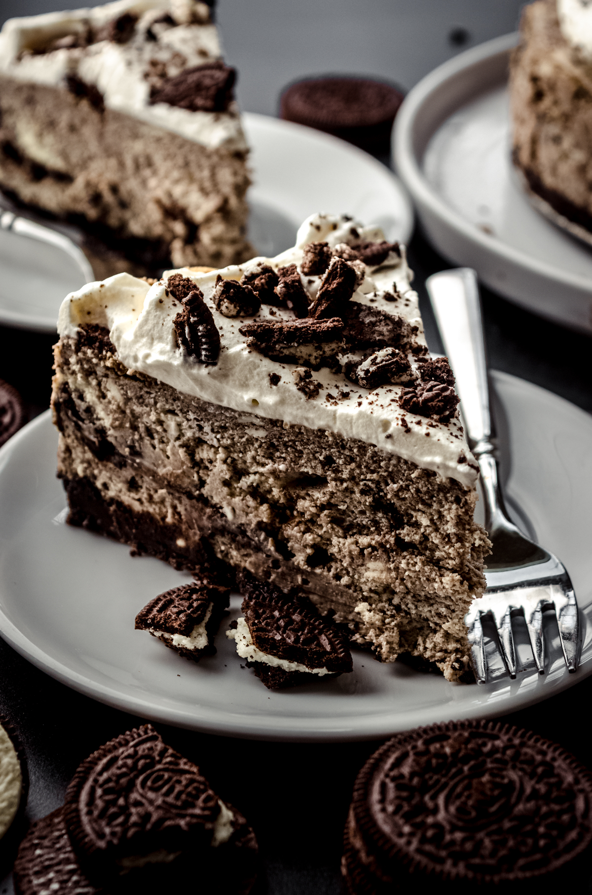 A slice of cookies and cream cheesecake on a plate with a fork and Oreo chunks.