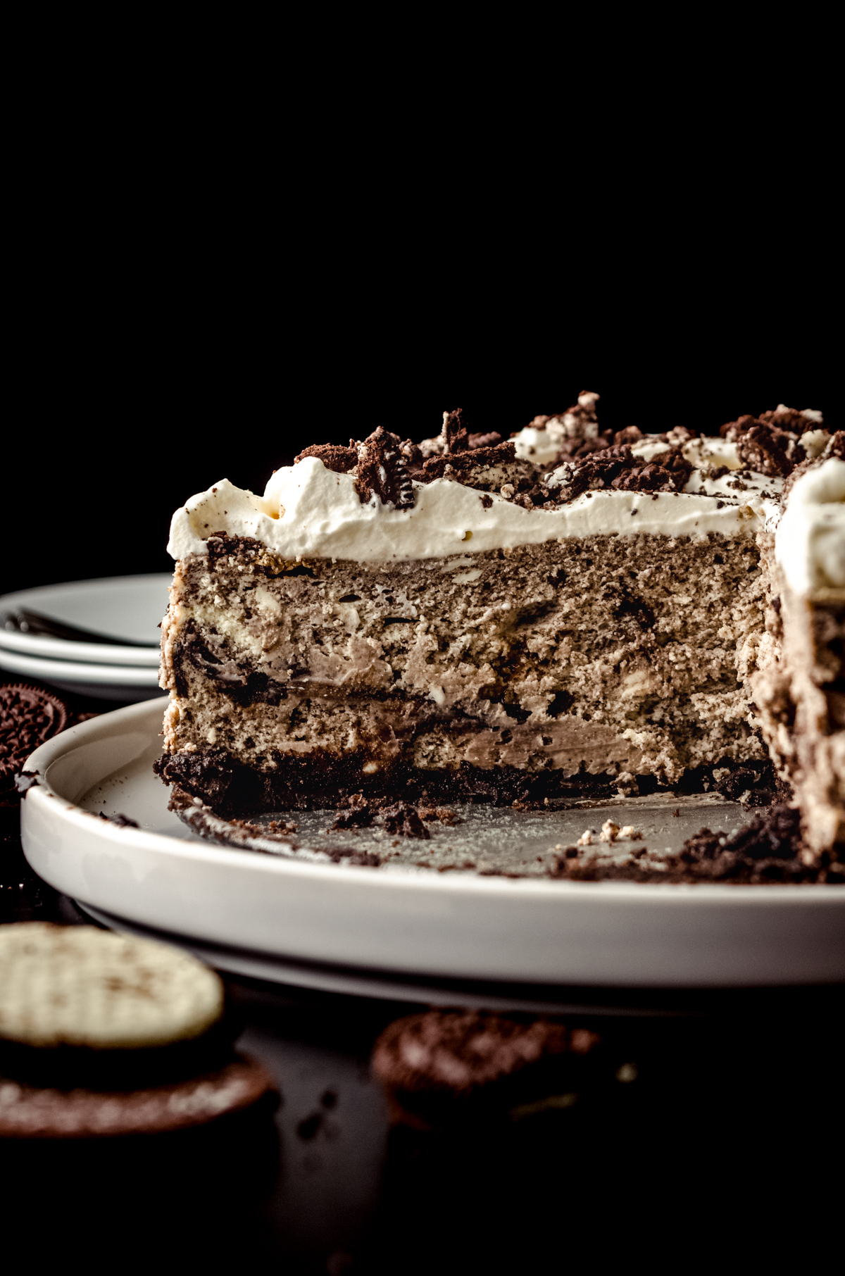 A cookies and cream cheesecake on a plate that has been sliced so you can see the cross-section of the cheesecake.