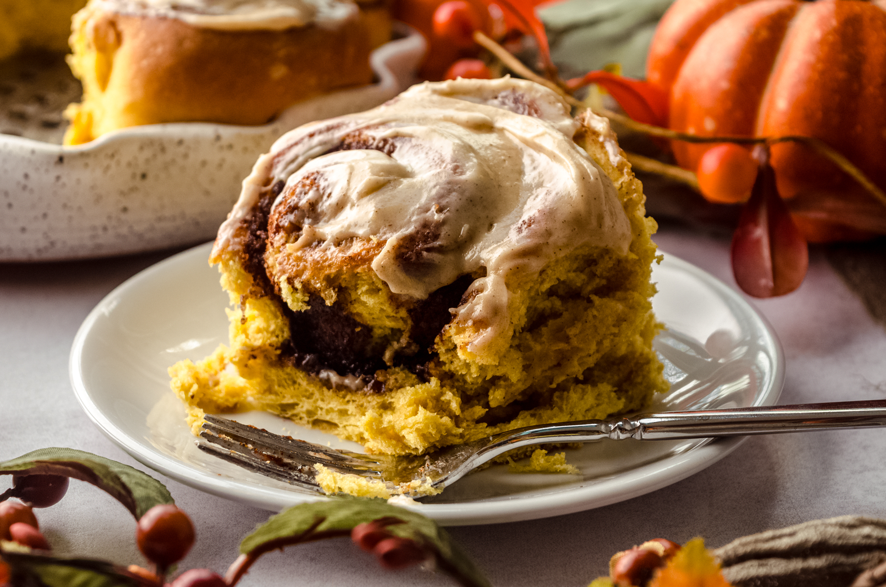 A pumpkin cinnamon roll on a plate with a fork and a bite taken out of it.