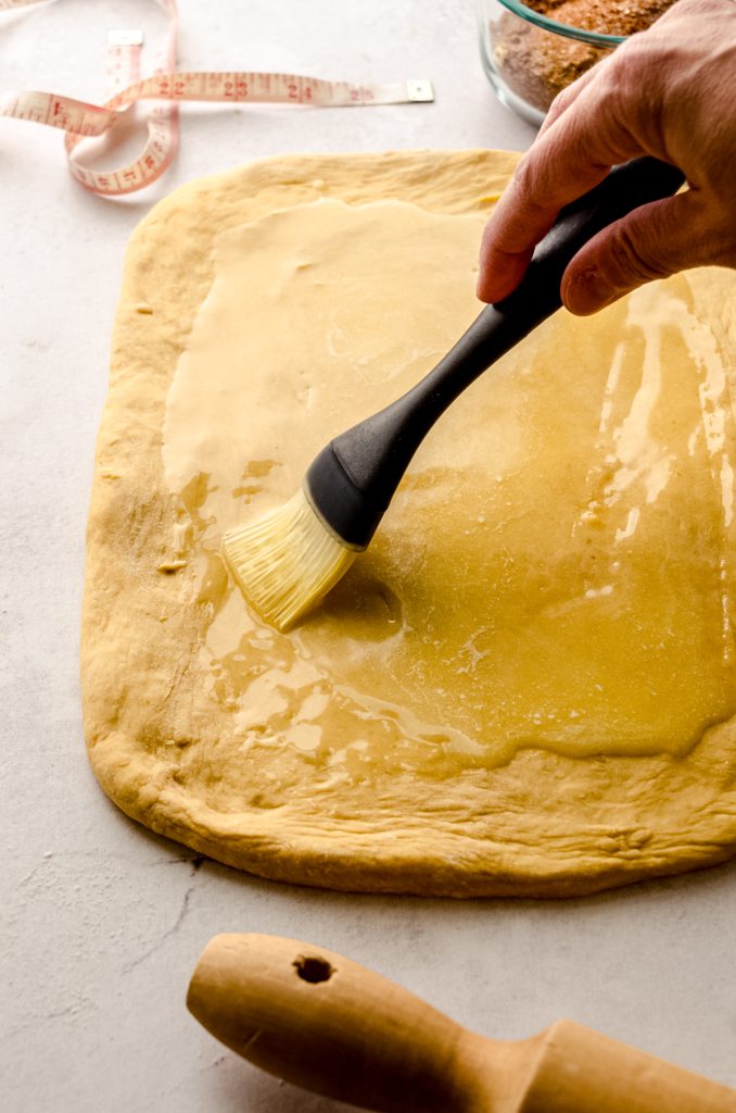 Someone is brushing melted butter onto a rectangle of dough to make pumpkin cinnamon rolls.