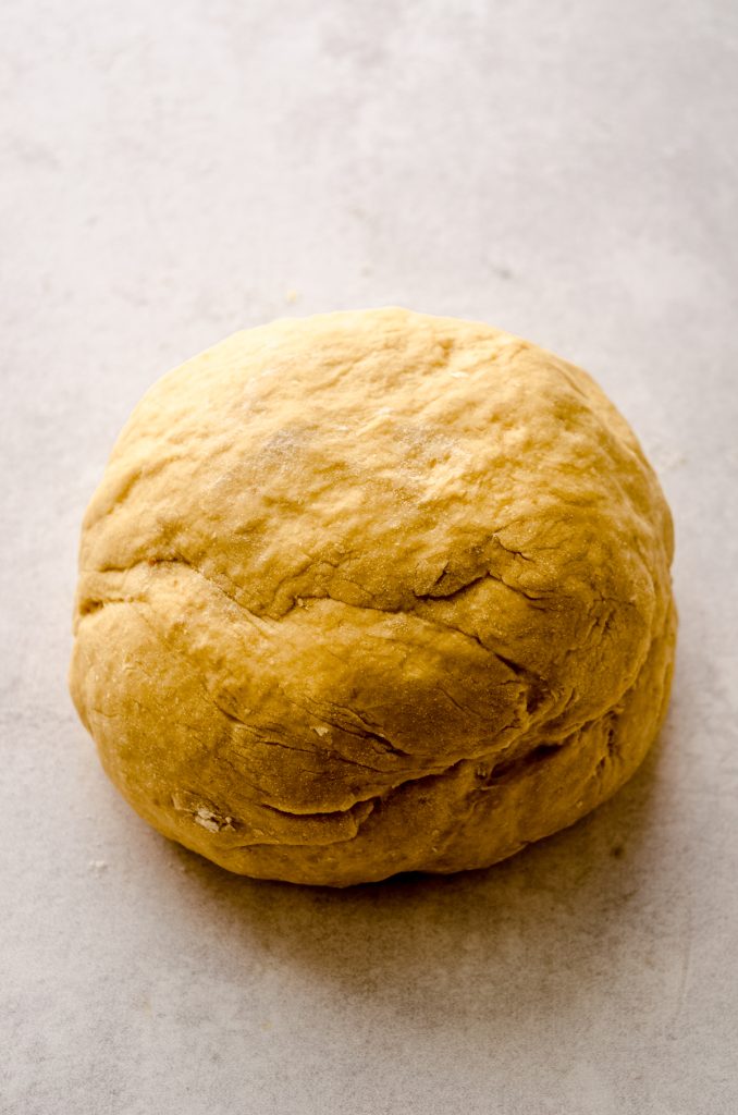 A ball of pumpkin cinnamon roll dough on a surface.