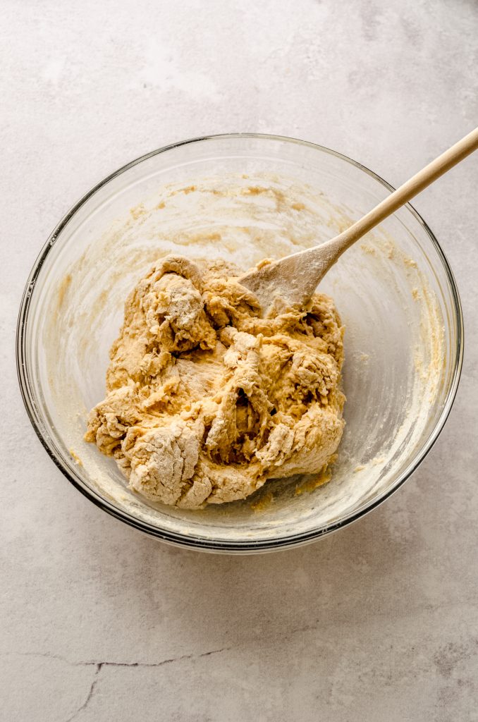 A progress photo of the ingredients make pumpkin cinnamon rolls being mixed in a large bowl with a wooden spoon.