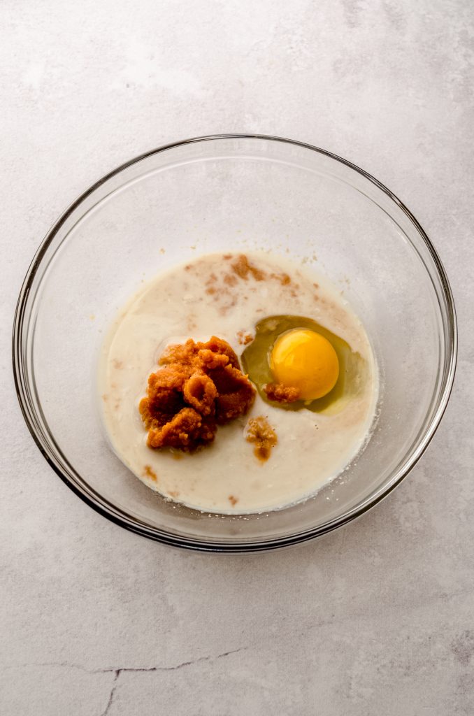 An egg, pumpkin, and wet ingredients in a large glass bowl to make pumpkin cinnamon rolls.