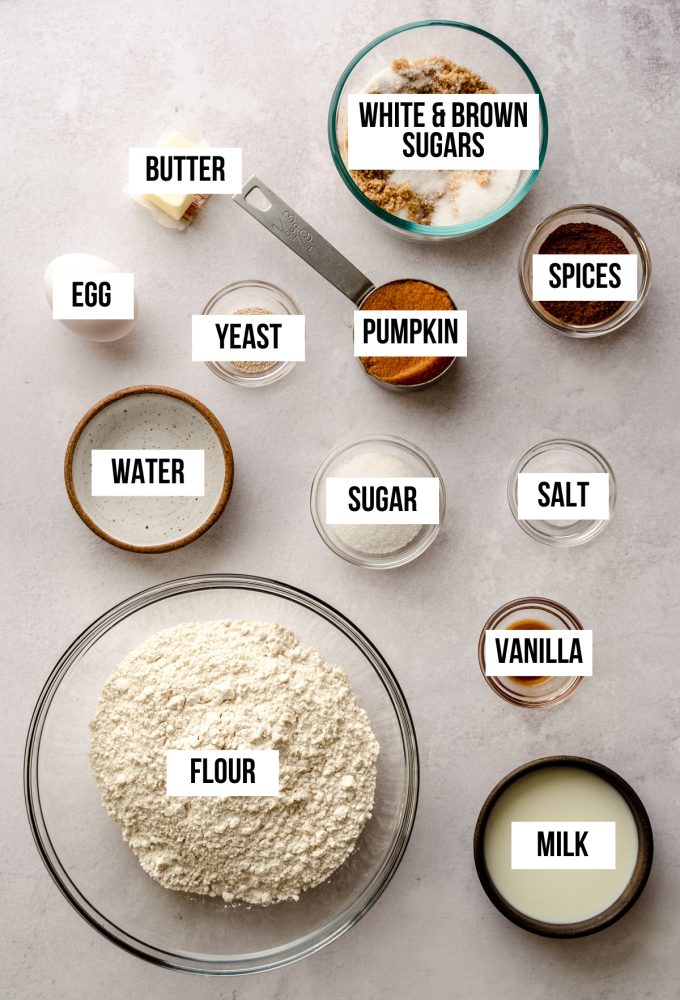 Aerial photo of ingredients to make pumpkin cinnamon rolls with text overlay labeling each ingredient. 