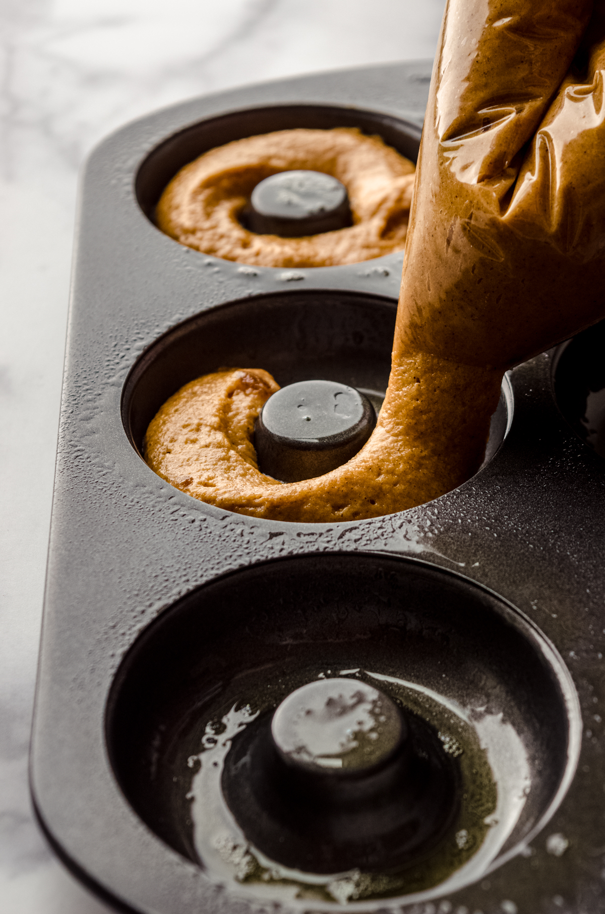 Someone is piping pumpkin donut batter into a donut pan.