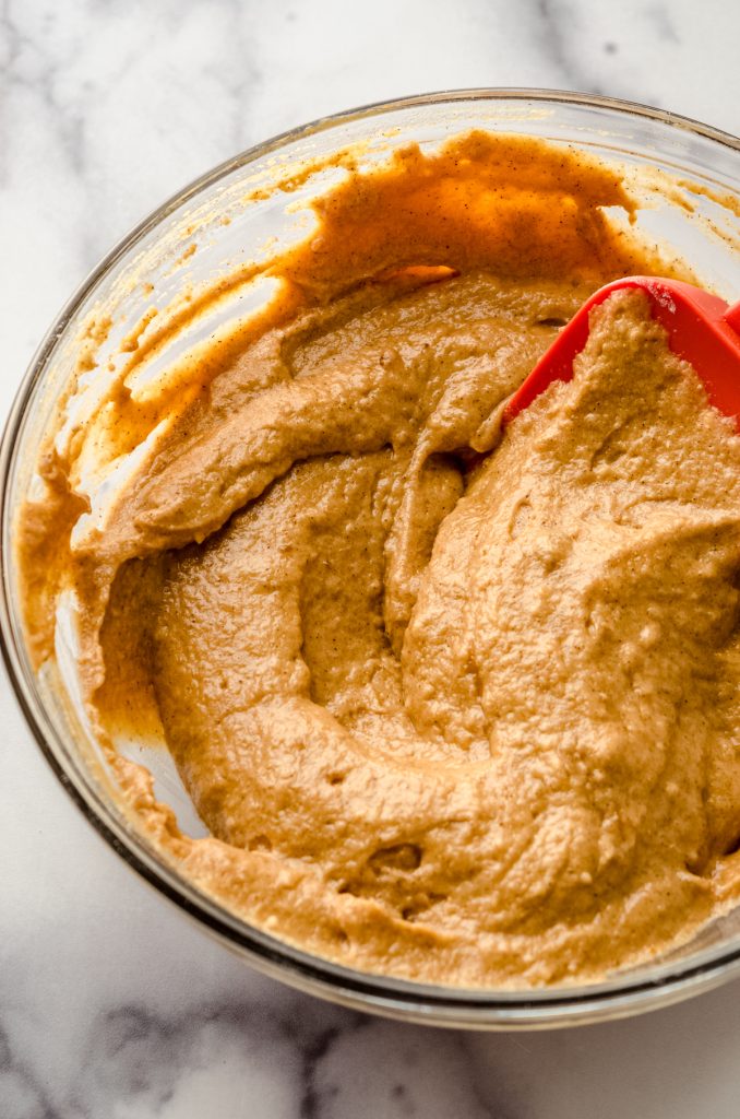 A spatula in a glass bowl mixing together the ingredients to make pumpkin donuts.